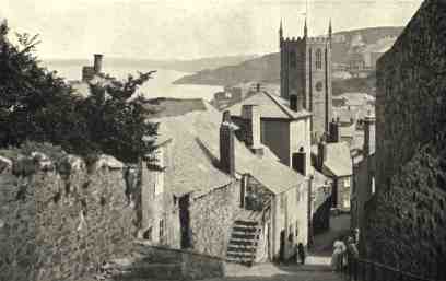 Looking down a steep hill with the church at the bottom and the bay in the distance